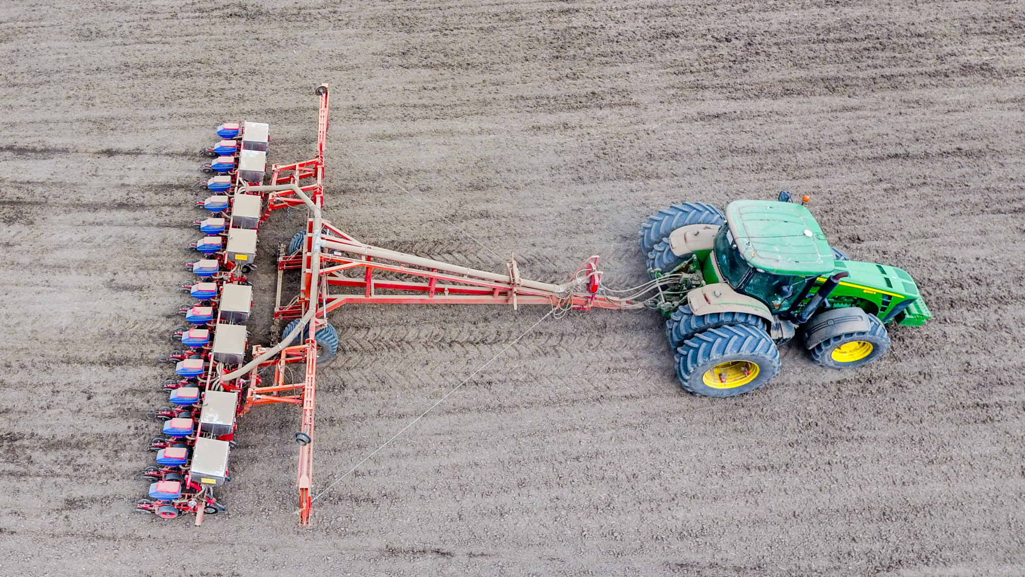 An aerial view of a green tractor planing corn into a field 